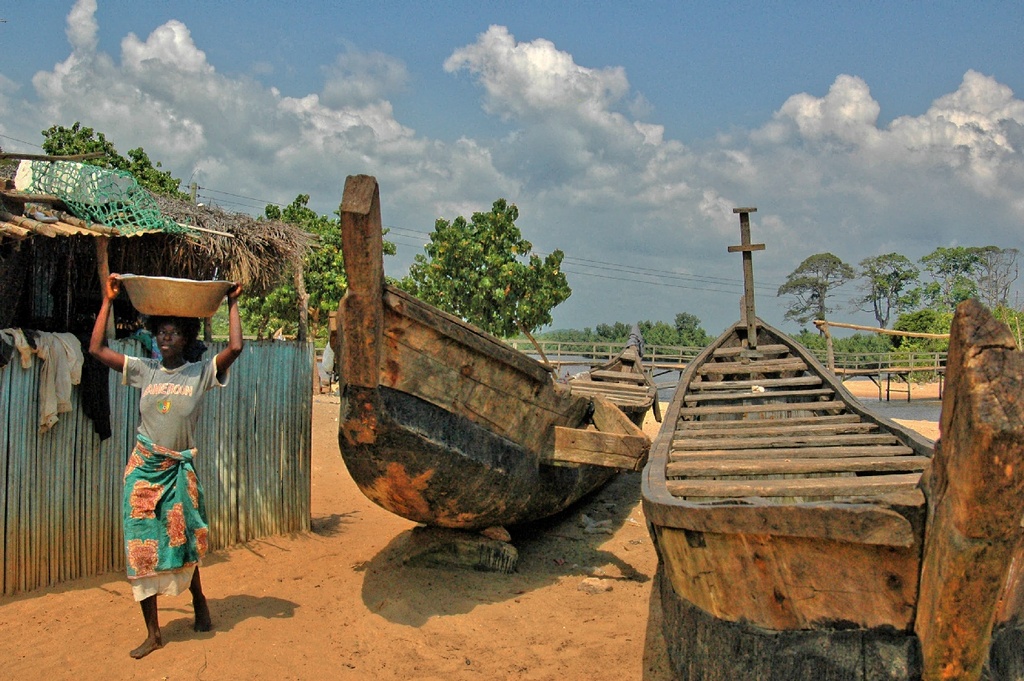 Butre with Fort batenstein. Ghana. Old fishing boats at the beach of Butre, and a woman passing by with a bowl on her head. Trave back in time!